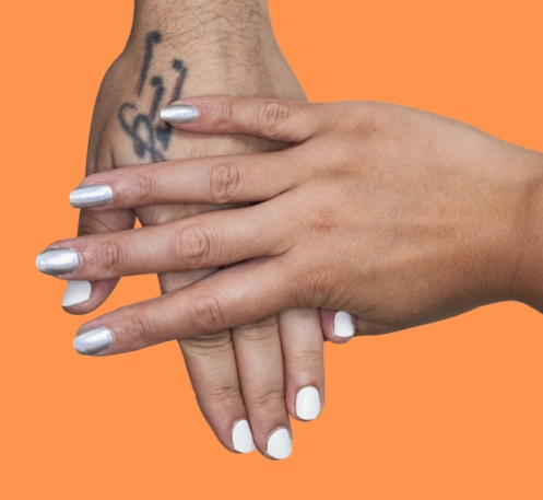 silver chrome gel nail wraps on female hand resting on white gel nail wraps on male hand against an orange background